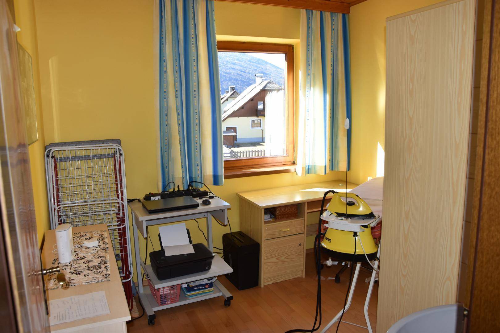 Mehrzweckraum mit Schreibtisch, Bügeleisen und Fenster, das Tageslicht spendet.