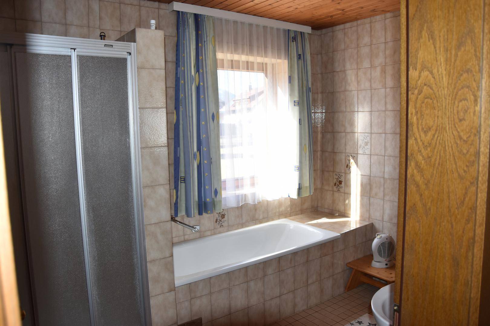 Badezimmer mit Duschkabine, Badewanne und Fenster, das viel Tageslicht hereinlässt.