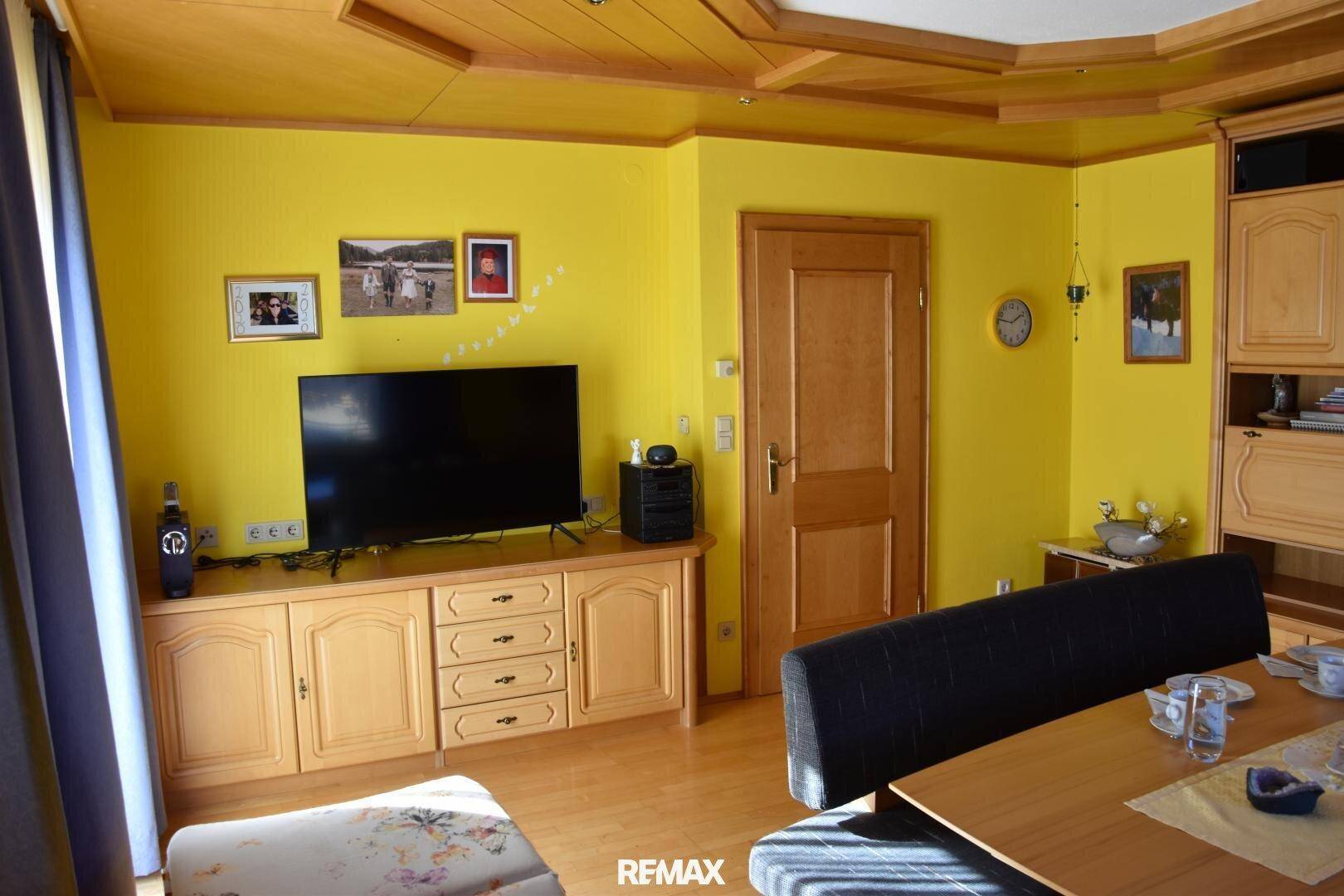Wohnzimmer mit gelben Wänden, Holzmöbeln und Fernseher, in traditionellem Stil.