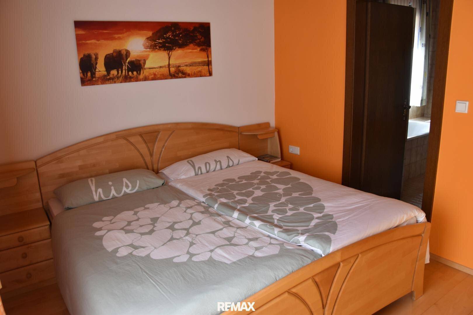 Schlafzimmer mit Doppelbett, Holzrahmen und orangefarbenen Wänden in gemütlicher Atmosphäre.