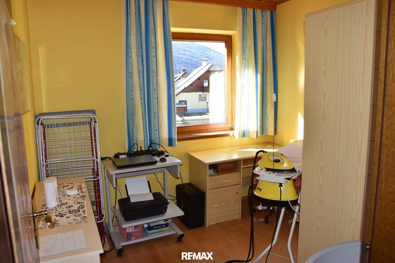 Arbeitszimmer mit Schreibtisch, Drucker und Fenster, hell und funktional eingerichtet.