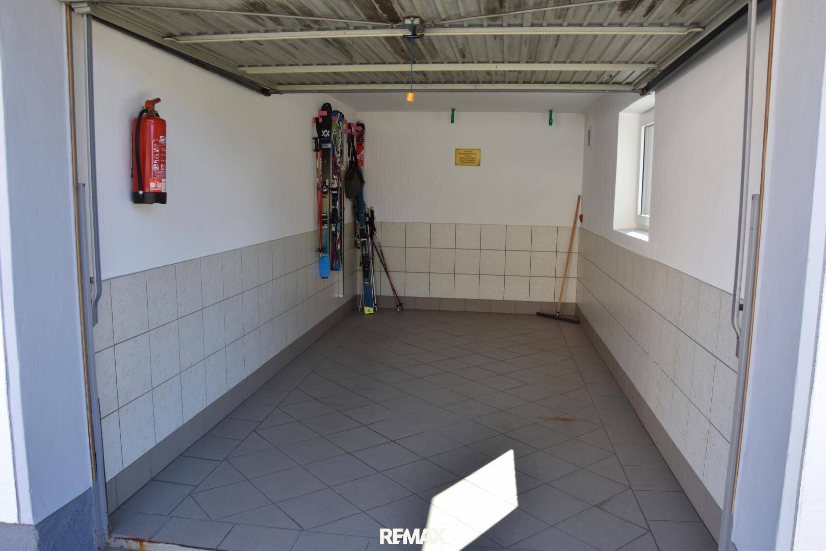 Geräumige Garage mit Fliesenboden und Fenster, bietet Platz für ein Fahrzeug und Sportgeräte.