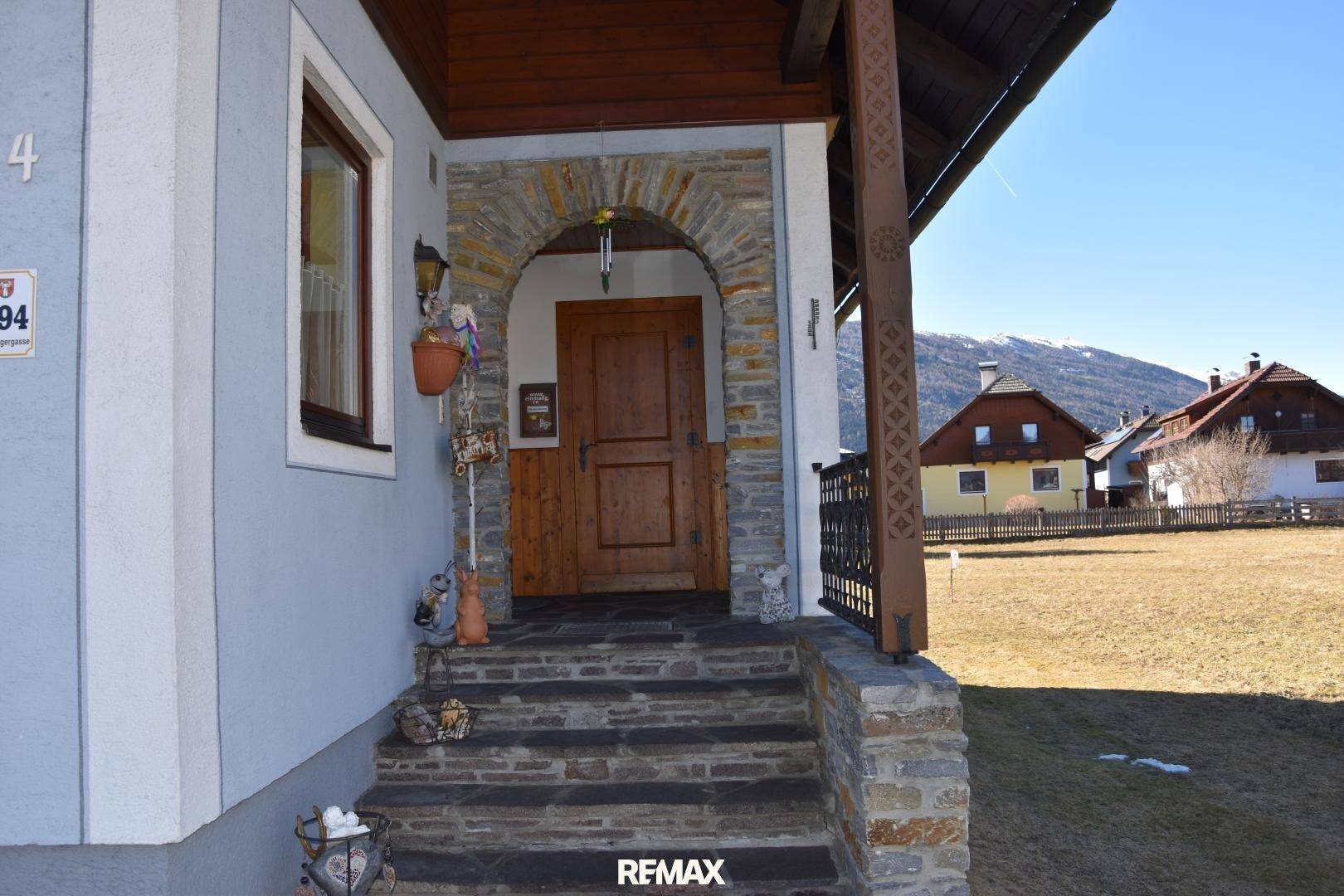 Eingangsbereich des Hauses mit Steintreppe und Holztür, umgeben von alpiner Landschaft.