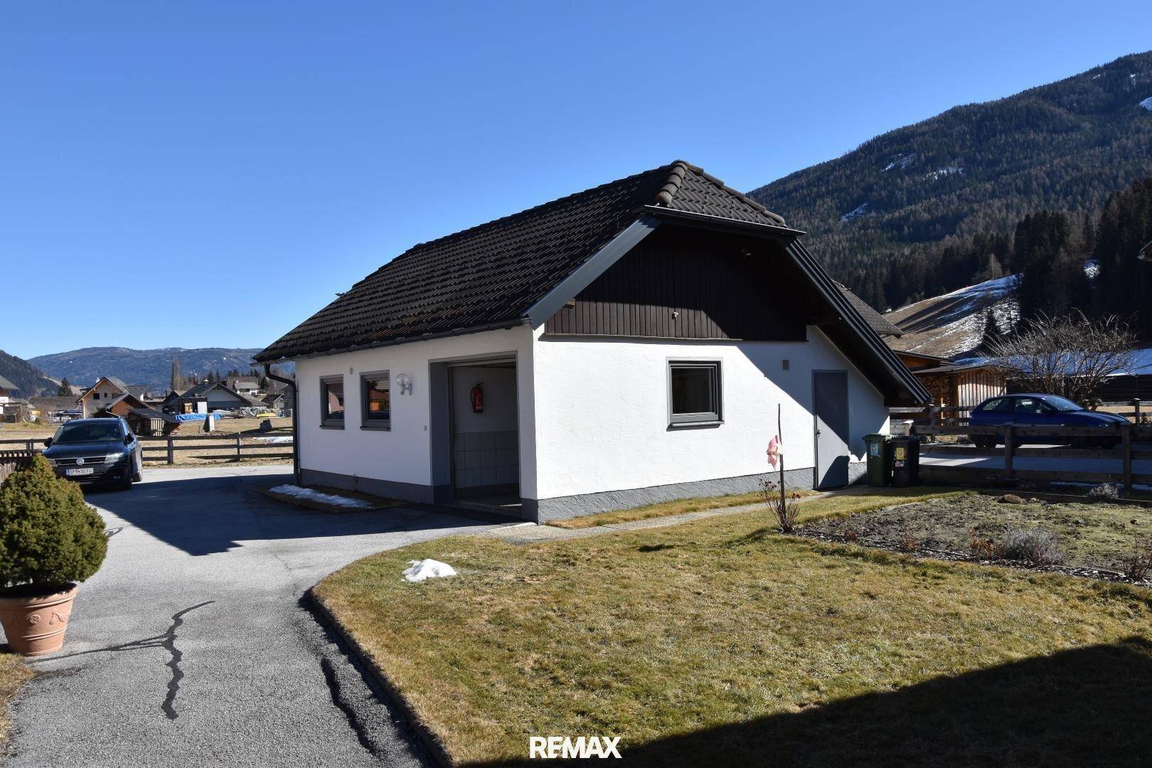 Weißes Einfamilienhaus mit dunklem Satteldach, integrierter Garage und gepflegtem Vorgarten.