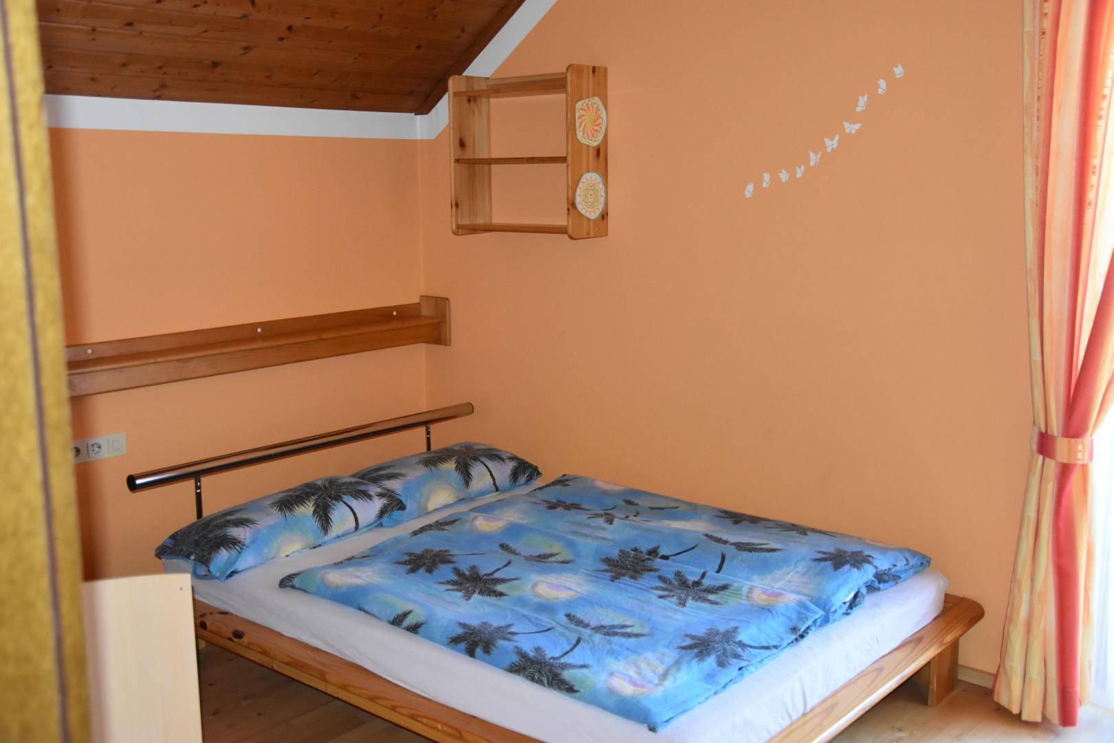 Schlafzimmer im Dachgeschoss mit Holzbett, orangefarbenen Wänden und Dachschräge.