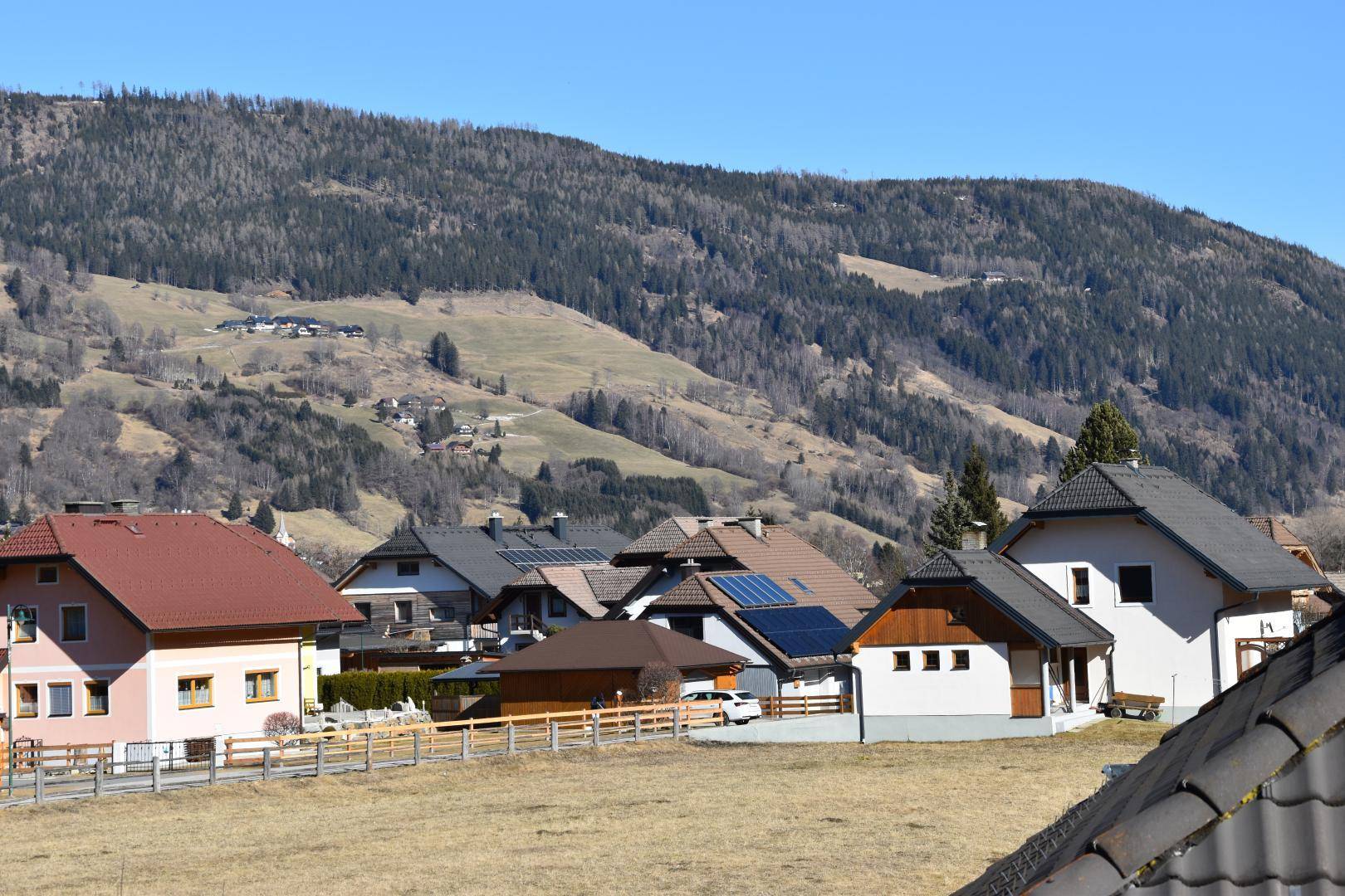 Panoramablick auf die ländliche Umgebung mit Wohnhäusern und bewaldeten Bergen im Hintergrund.