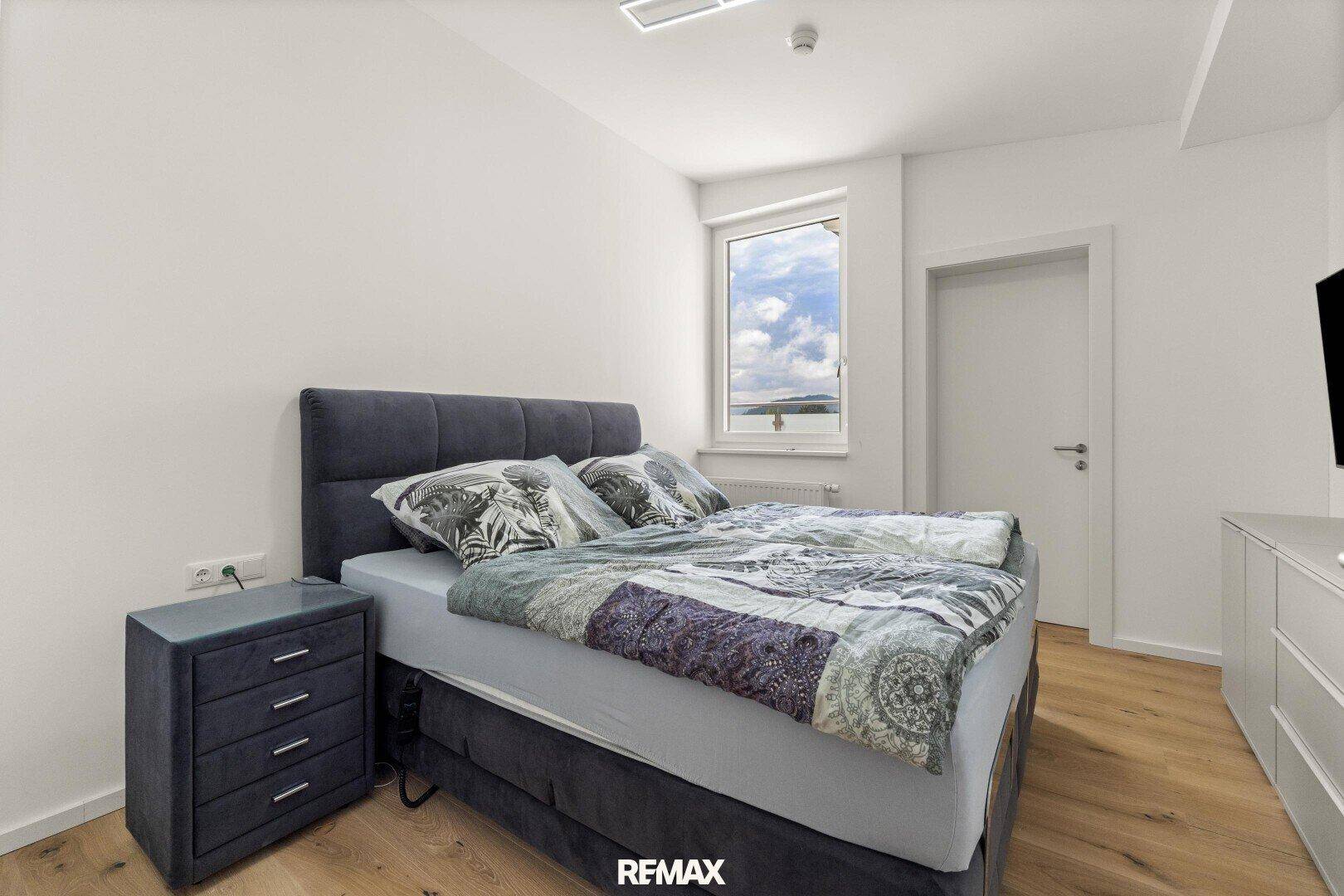 Modernes Schlafzimmer mit Boxspringbett, Nachttisch und Fenster mit Ausblick.