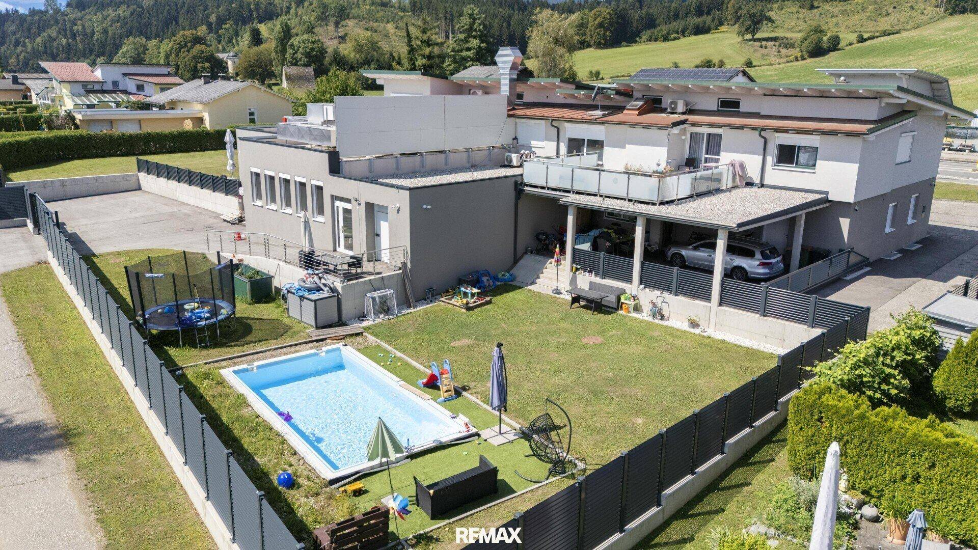 Großer Garten mit Swimmingpool, Rasenfläche und Spielgeräten für Kinder.