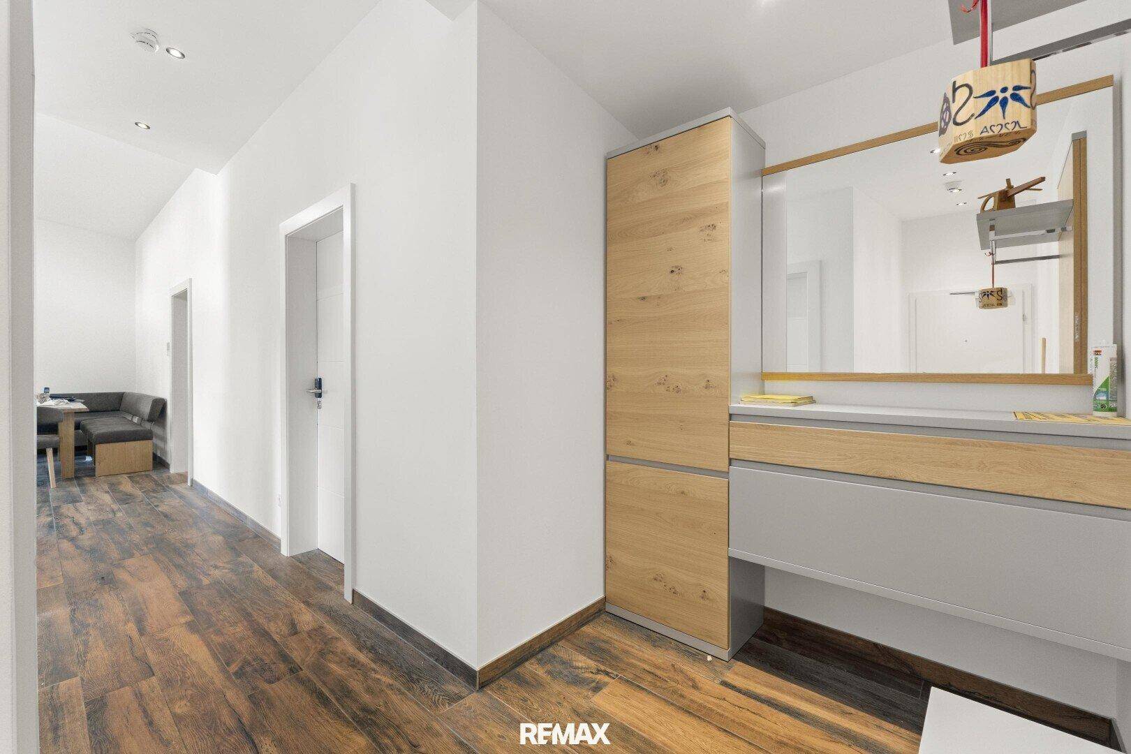 Heller Flur mit Holzboden, Garderobe und Spiegel, der zu weiteren Räumen führt.