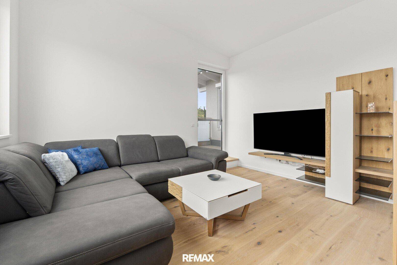 Gemütliches Wohnzimmer mit großem Sofa, Fernseher und Zugang zu einem Balkon.