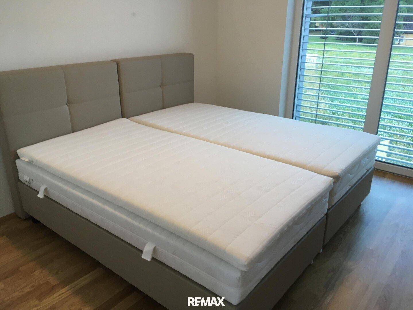 Helles Schlafzimmer mit Doppelbett, Holzboden und großen Fenstern mit Blick ins Grüne.