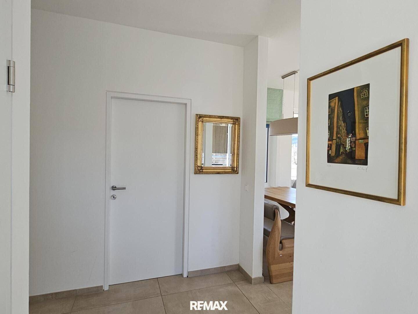Heller Flur mit weißer Tür, einem dekorativen Spiegel und Kunst an der Wand.