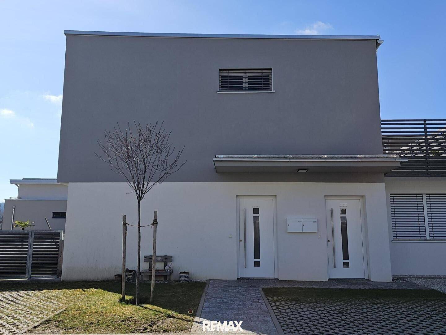 Moderne Doppelhaushälfte mit grauer und weißer Fassade und kleinem Vorgarten.