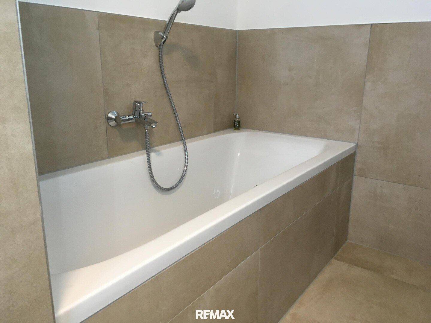 Eingebaute Badewanne mit Handbrause in einem modern gefliesten Badezimmer.