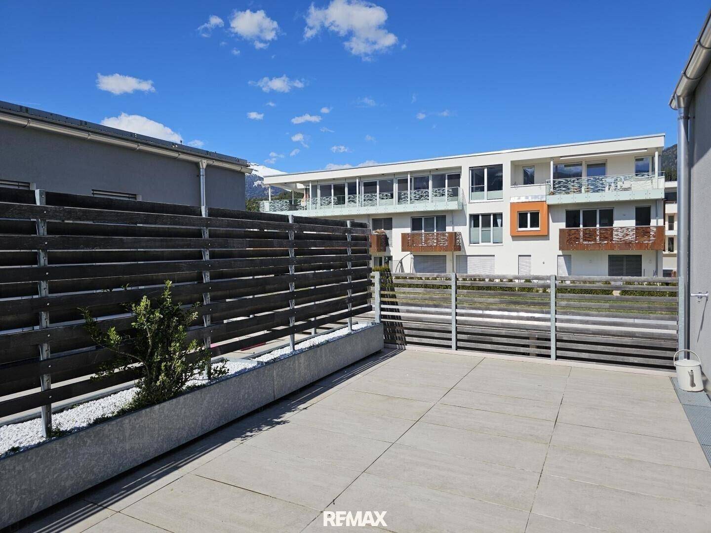 Große, sonnige Terrasse mit Steinplatten und dekorativen Pflanzenkübeln.