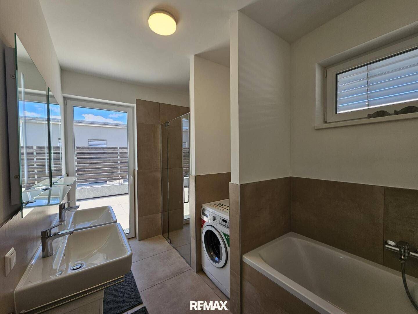 Modernes Badezimmer mit Doppelwaschbecken, Badewanne, Dusche und Waschmaschine.