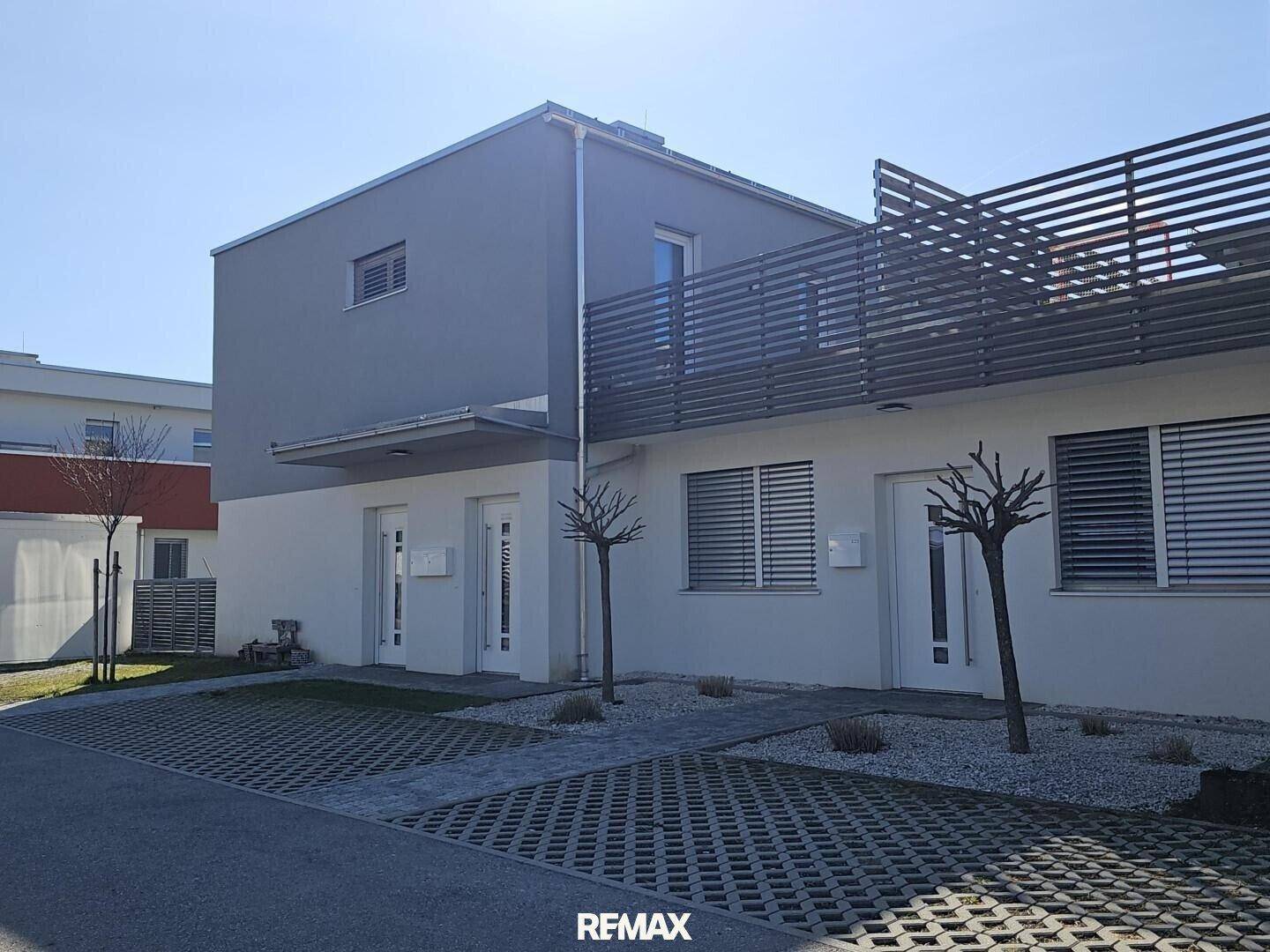 Moderne Doppelhaushälfte mit grauer und weißer Fassade und gepflastertem Vorplatz.