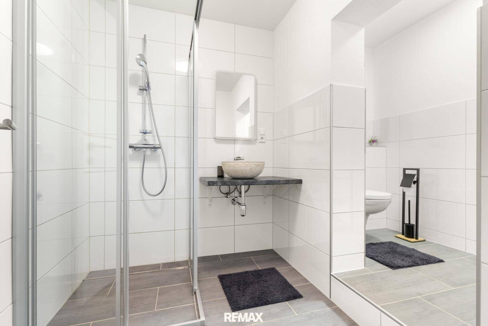 Modernes Badezimmer mit großer Dusche und separatem WC-Bereich, hell gefliest.