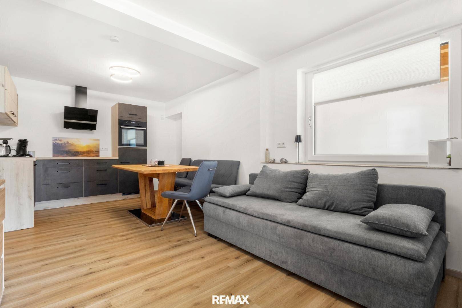 Offener Wohn- und Essbereich mit integrierter Küche, modernem Sofa und Holzboden.