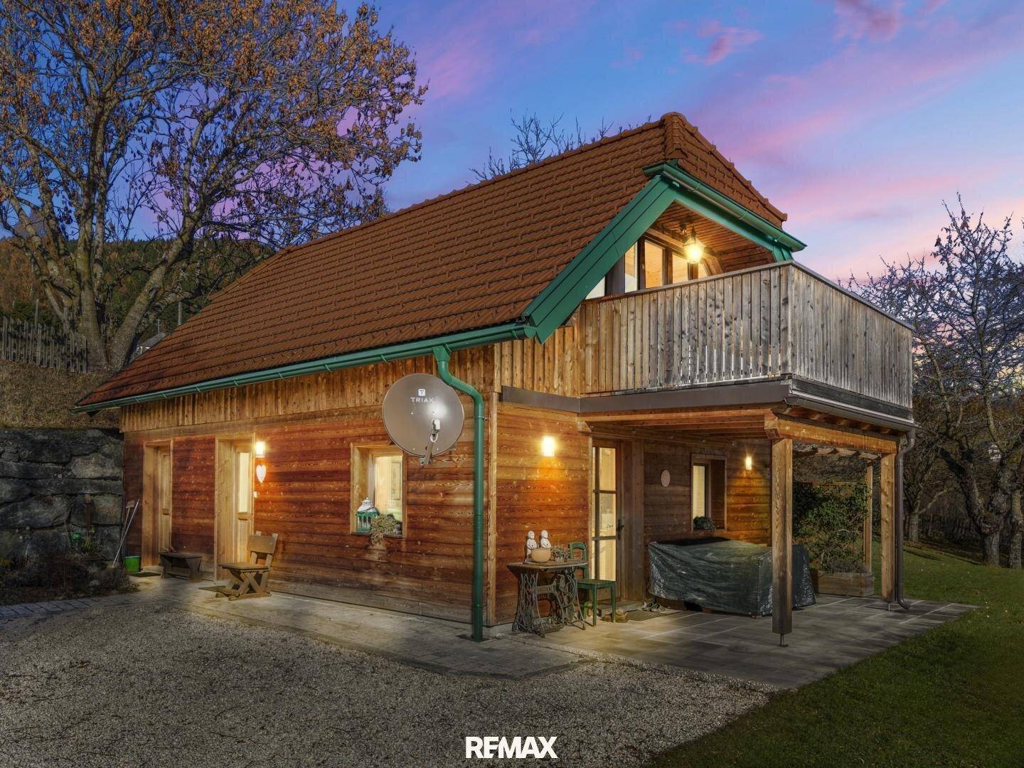 Holzhaus bei Dämmerung mit beleuchtetem Balkon und überdachtem Terrassenbereich.