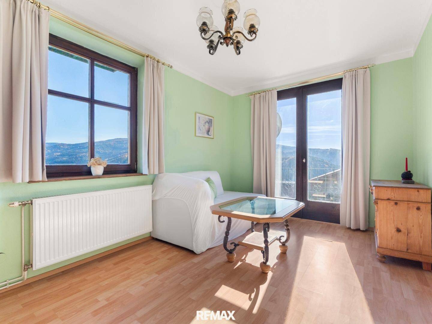 Helles Wohnzimmer mit hellgrünen Wänden, Holzboden und Zugang zu einem Balkon mit Bergblick.