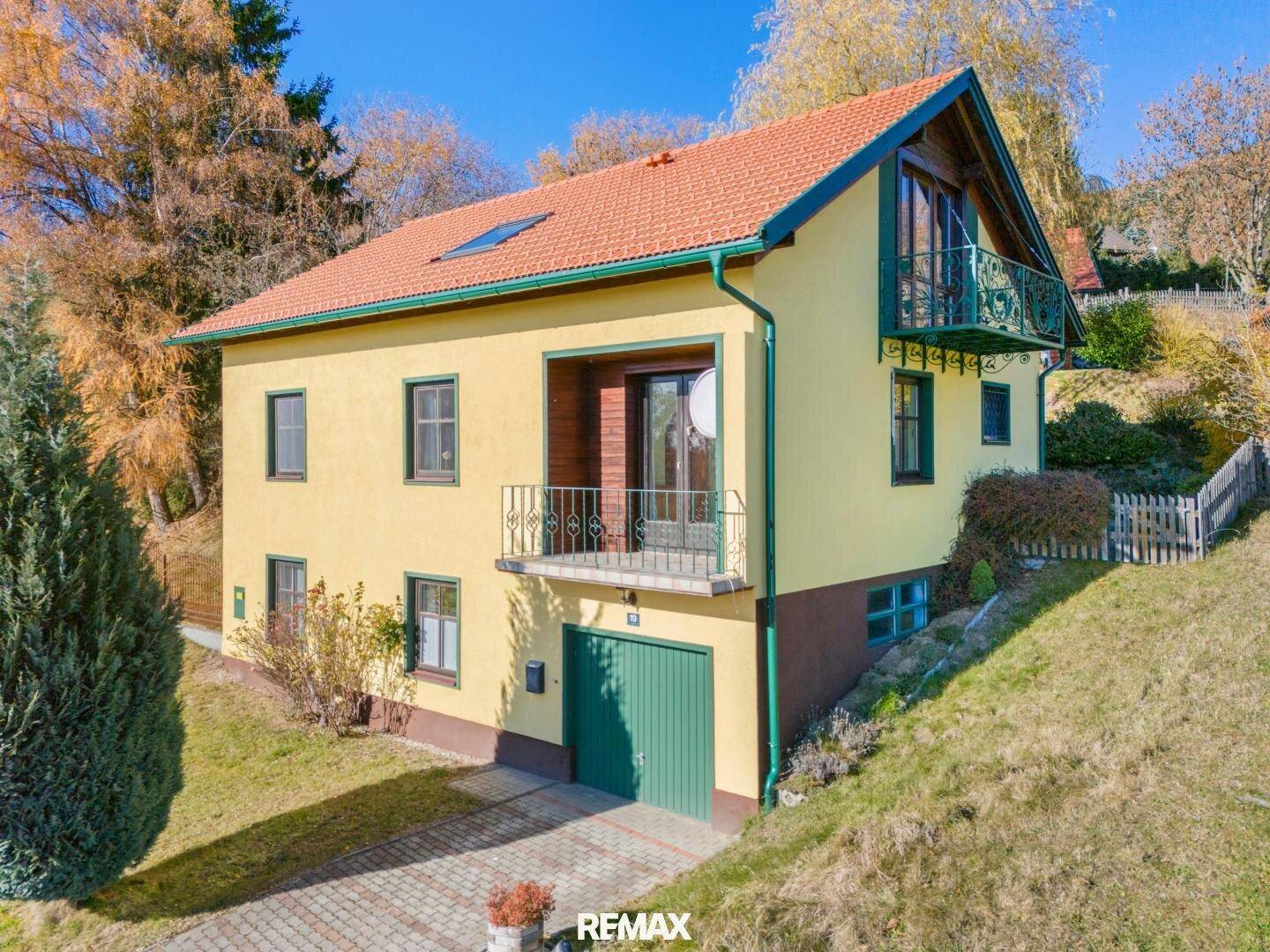 Gelbes Haus mit grüner Garage und Balkonen, eingebettet in eine Hanglage mit viel Grün.