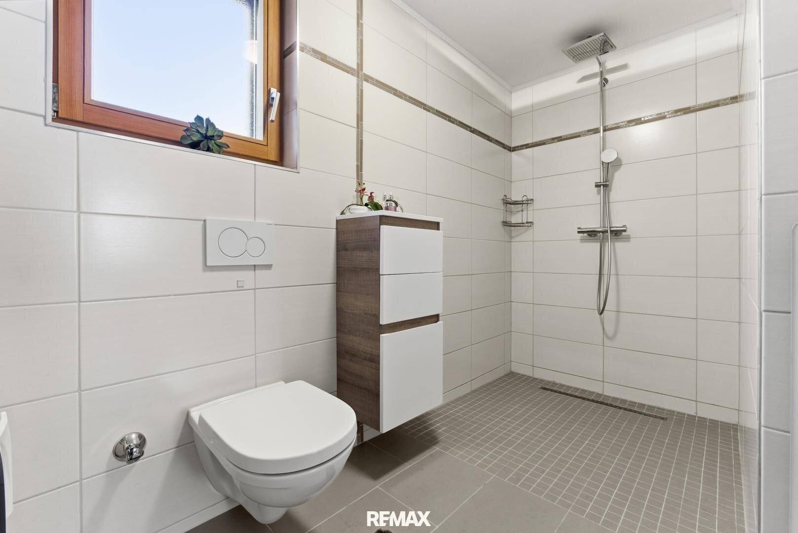 Modernes Badezimmer mit ebenerdiger Dusche, Wand-WC und Fenster für natürliches Tageslicht.