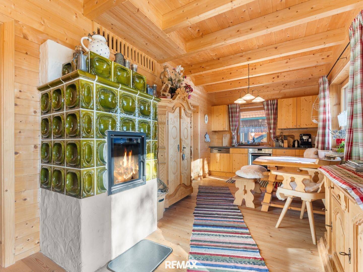 Gemütlicher alpiner Wohn-Essbereich mit grünem Kachelofen, Holzwänden und traditionellen Möbeln.