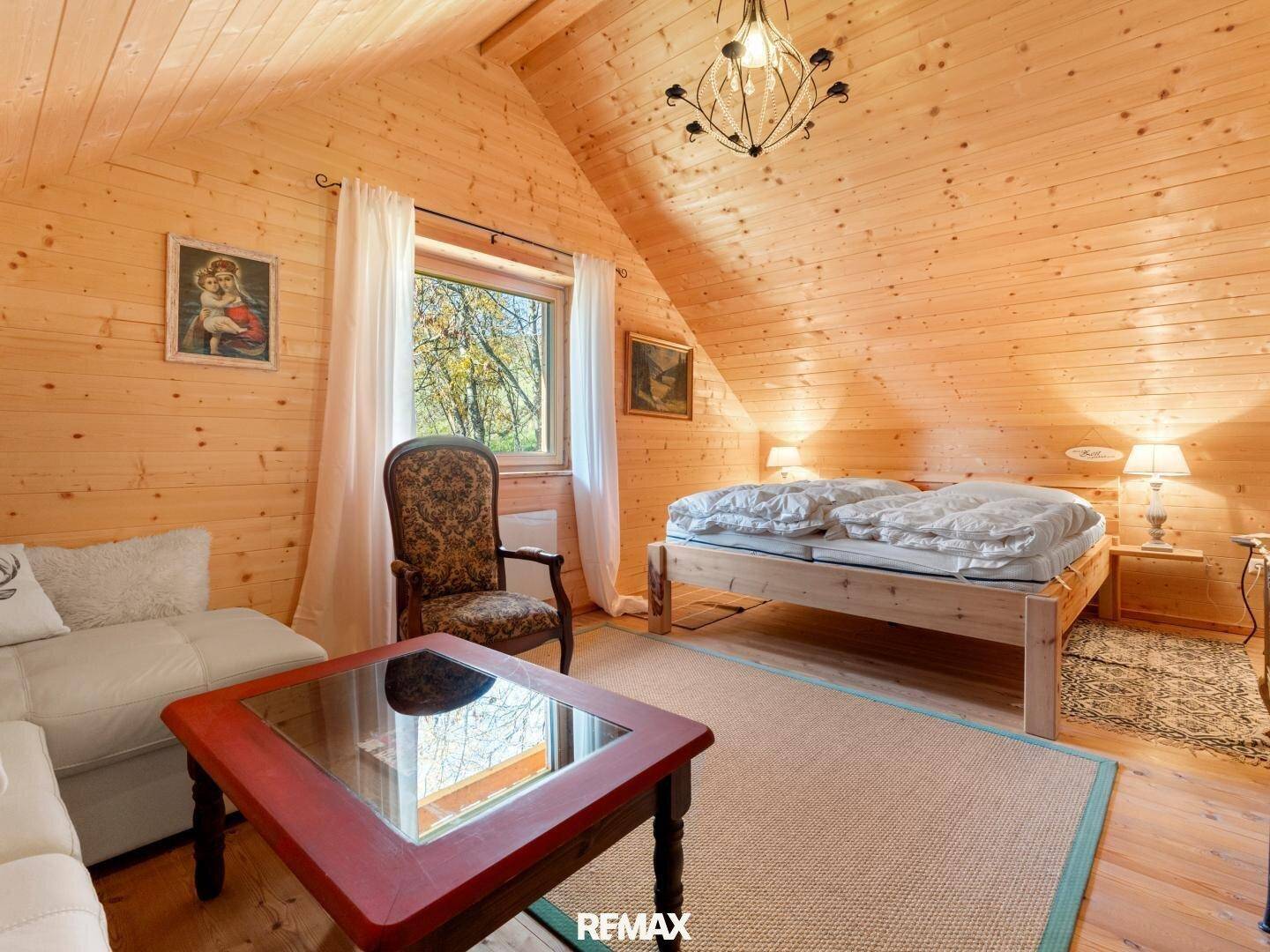Geräumiges Schlafzimmer im Dachgeschoss mit Holzwänden, Doppelbett und Sitzbereich.