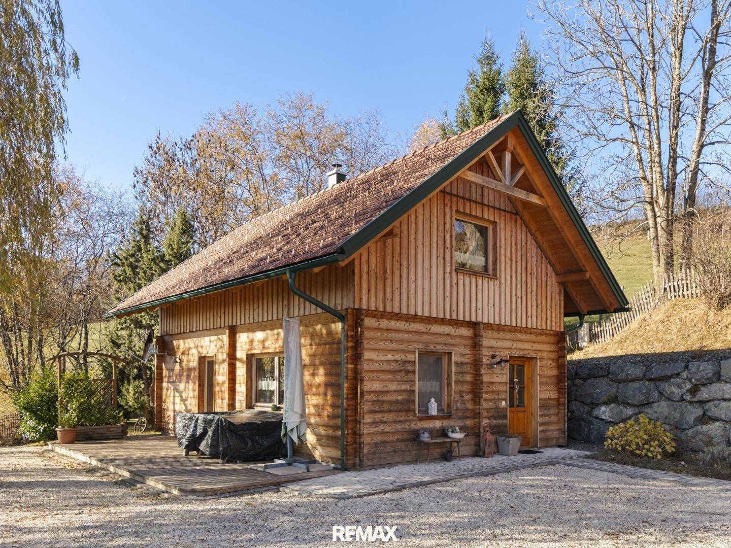 Rustikales Holzhaus mit kleiner Terrasse, Kiesauffahrt und einer Natursteinmauer.