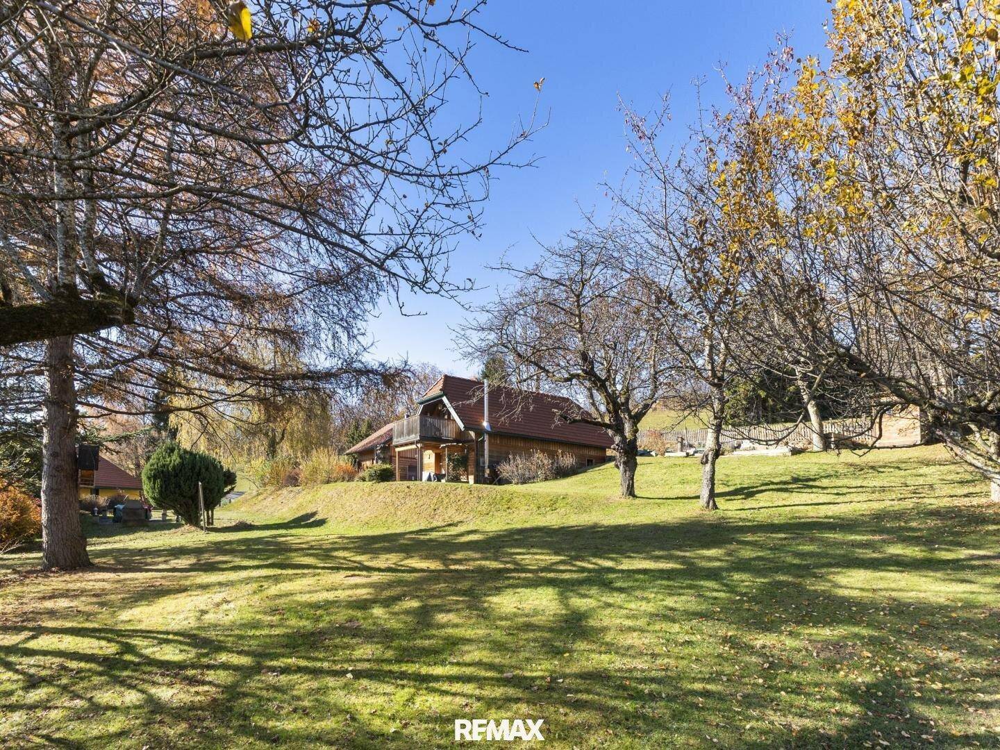 Haus auf einem Hügel mit großem Garten und vielen Bäumen unter blauem Himmel.