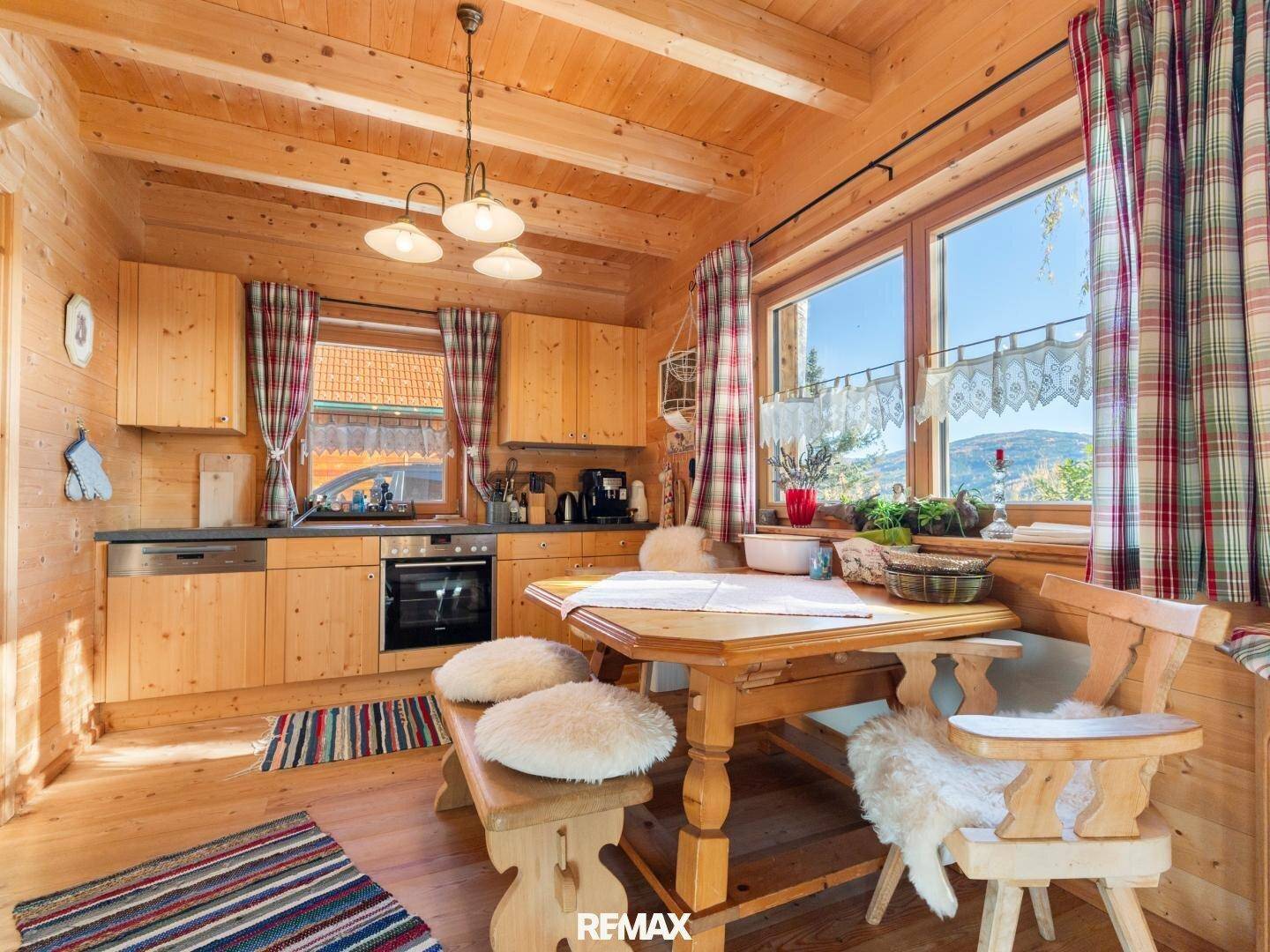 Helle Wohnküche in einem Holzhaus mit großen Fenstern, Holzküche und Essbereich.