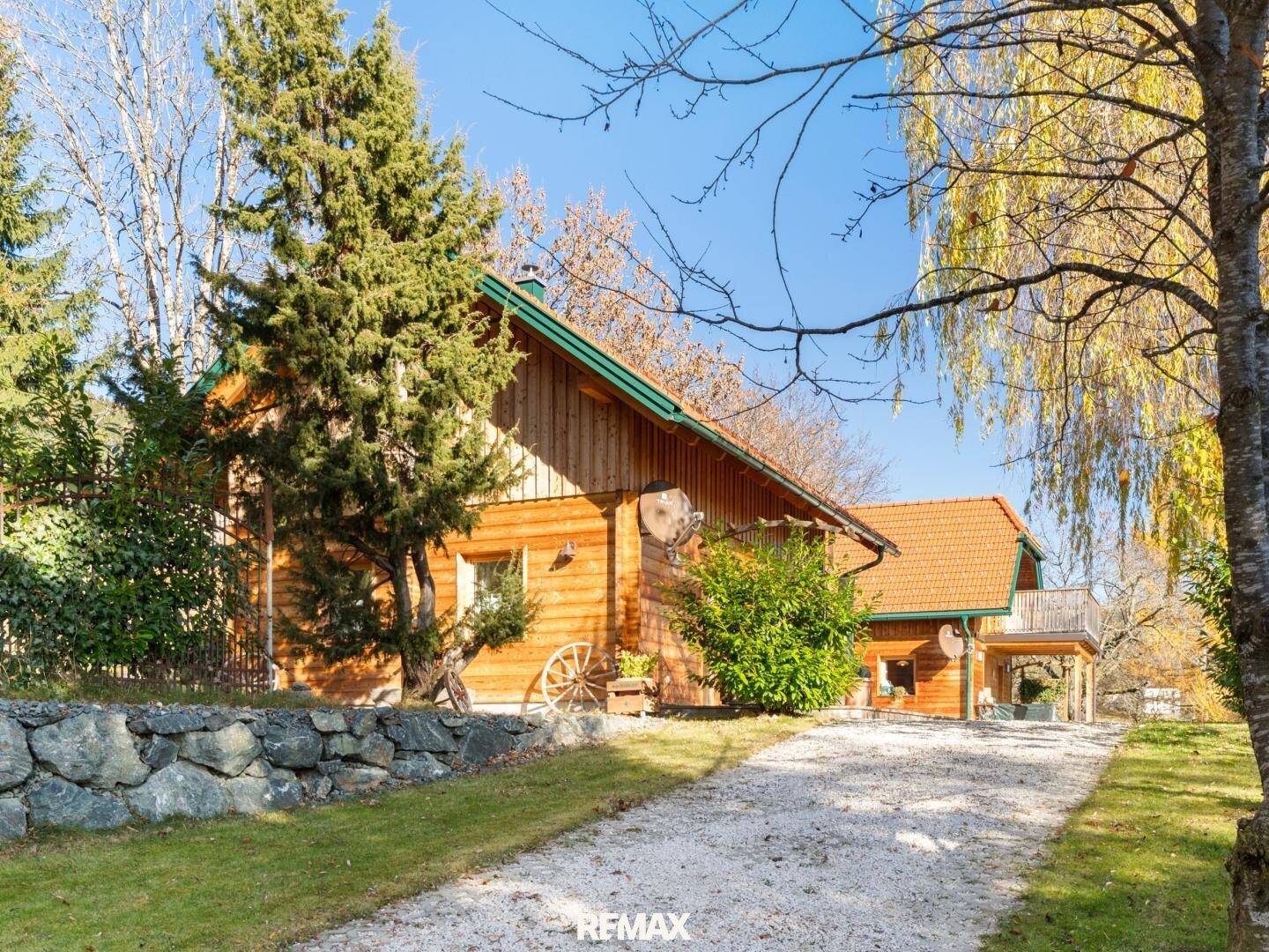 Charmantes Holzhaus mit Schindeldach, umgeben von Bäumen und einem Kiesweg.