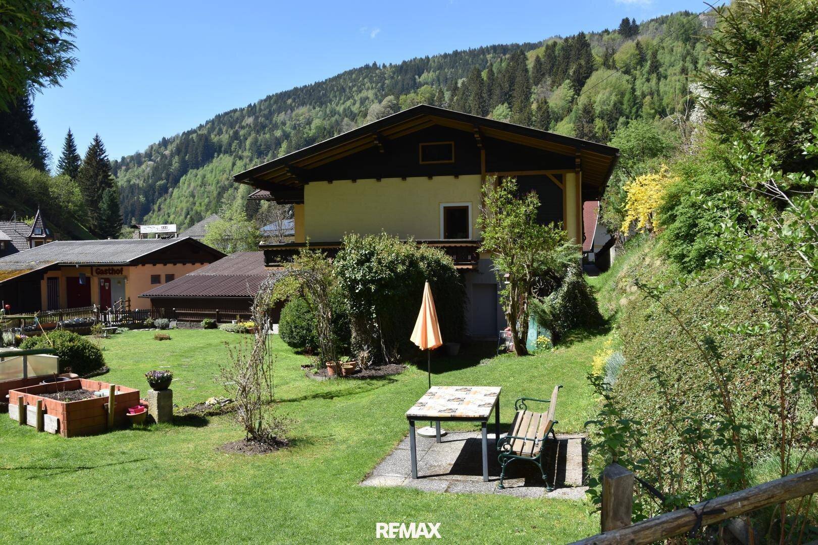 Gartenbereich mit Sitzgelegenheiten im Freien, Sonnenschirm und Blick auf das Haus.