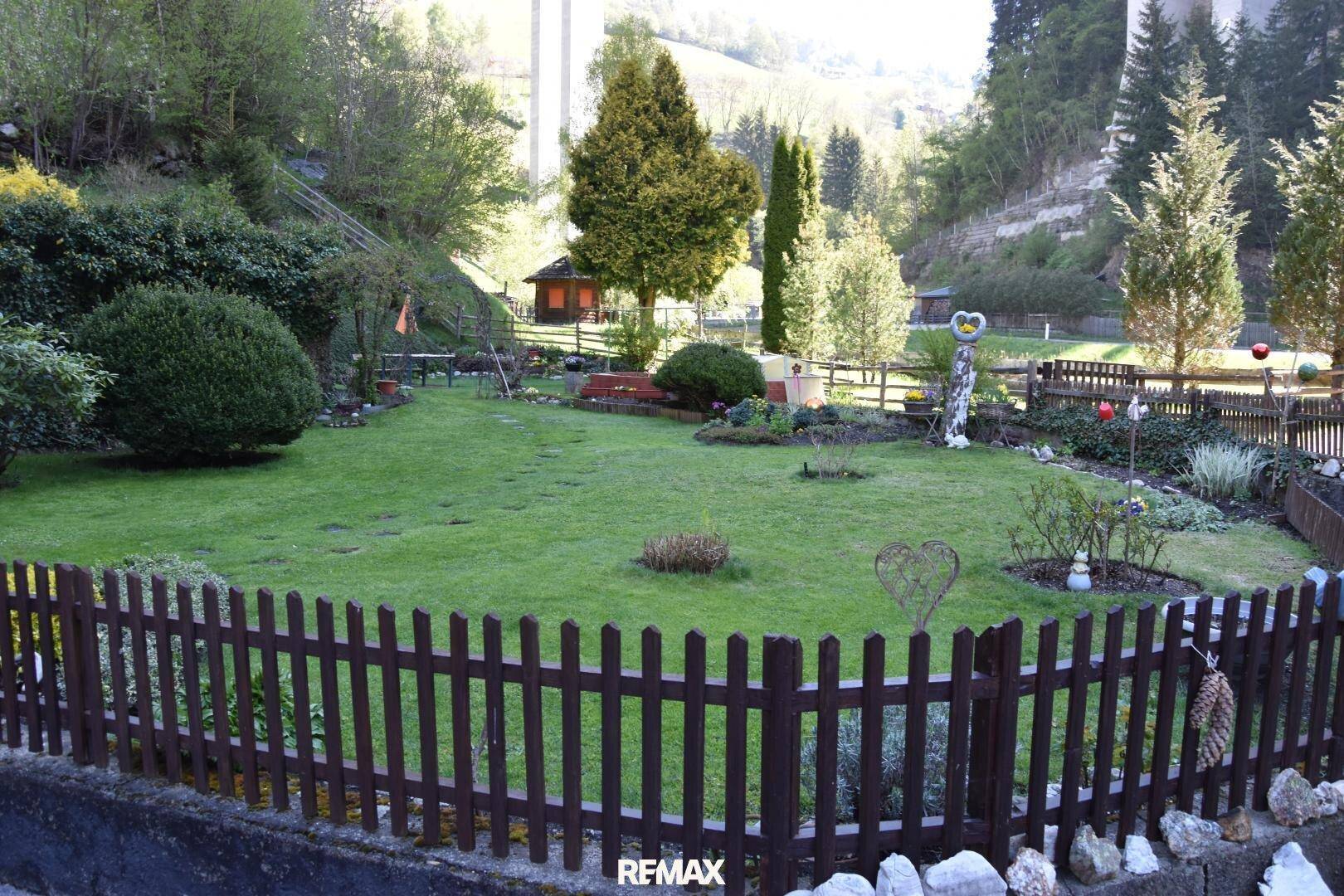 Weitläufiger Garten mit Holzzaun, gepflegtem Rasen und verschiedenen Pflanzen.