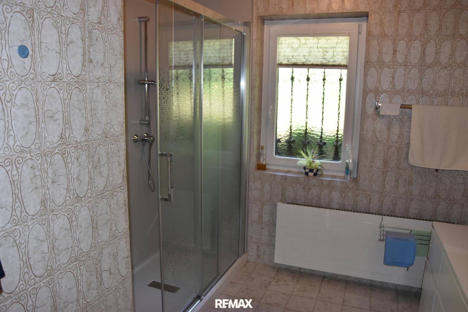 Badezimmer mit Duschkabine, gemusterten Fliesen und einem Fenster, das für Helligkeit sorgt.
