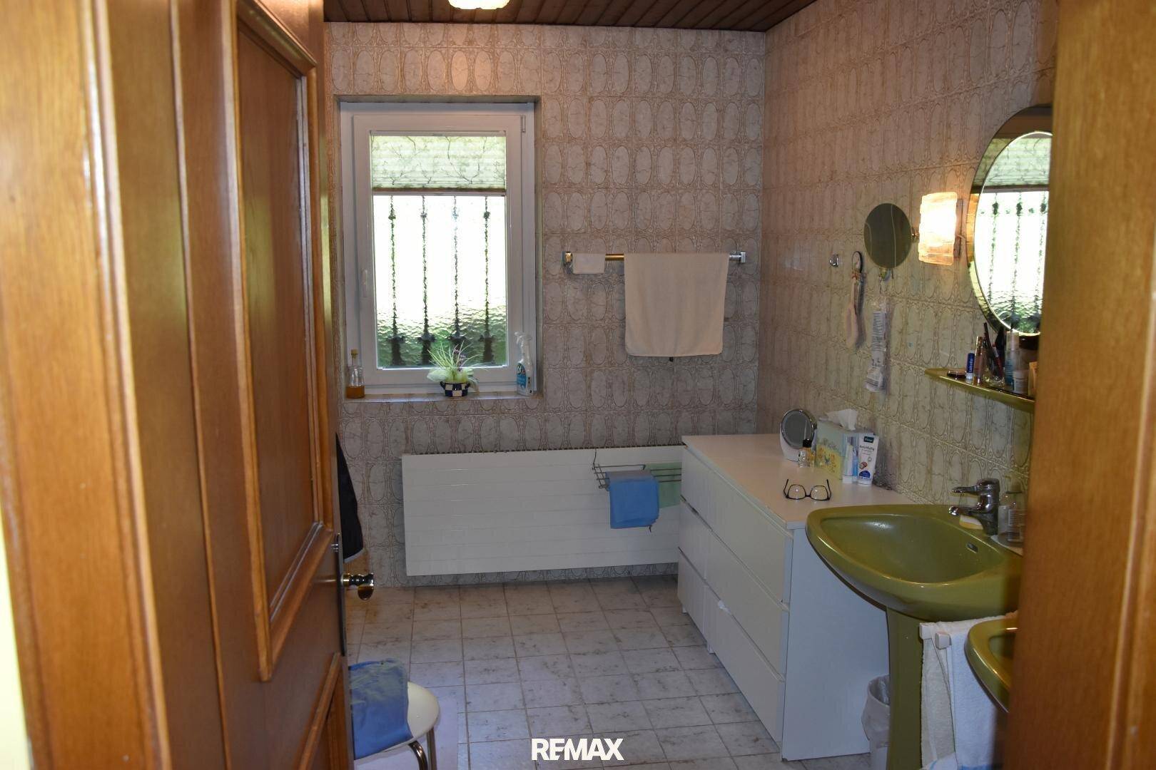 Badezimmer mit gemusterten Fliesen, grünem Waschbecken und einem Fenster für Tageslicht.