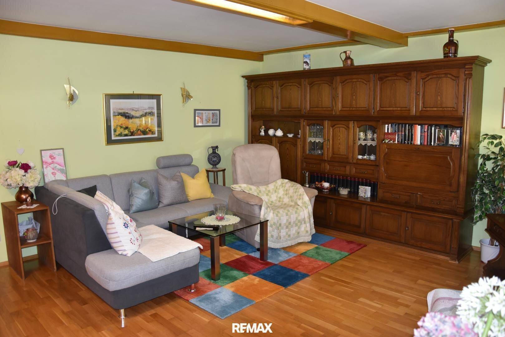 Gemütliches Wohnzimmer mit grauem Ecksofa, großer Holzschrankwand und Holzboden.