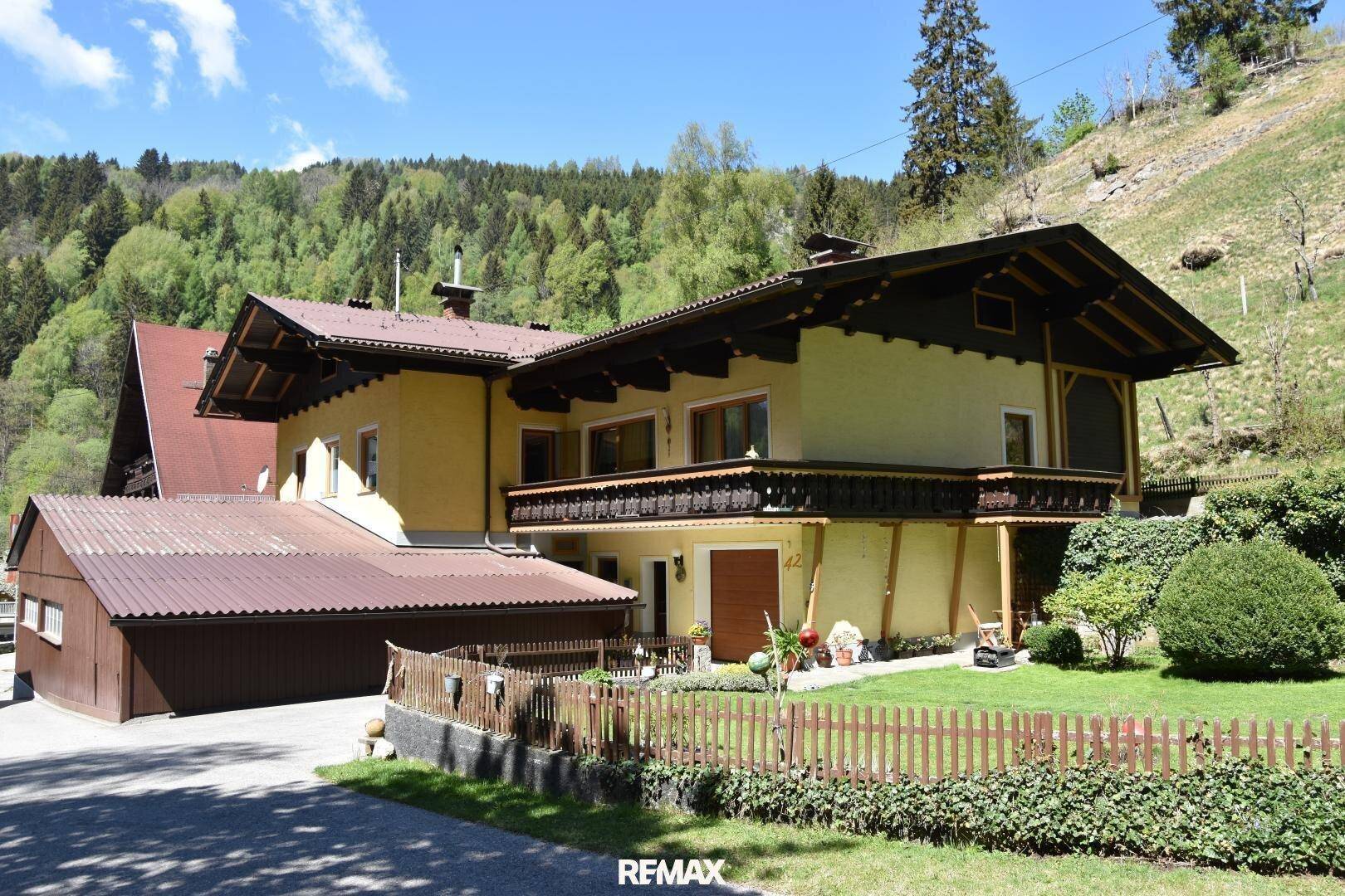 Traditionelles gelbes Haus mit Holzbalkon und gepflegtem Vorgarten in ländlicher Umgebung.