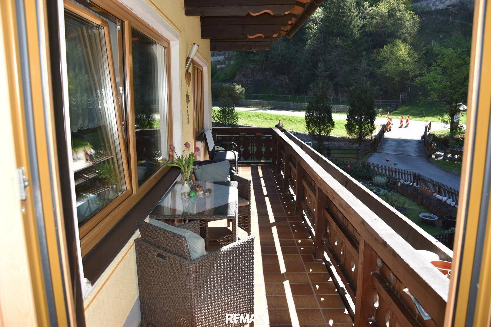 Sonniger Balkon mit Outdoor-Möbeln und Blick auf die grüne Umgebung und die Straße.