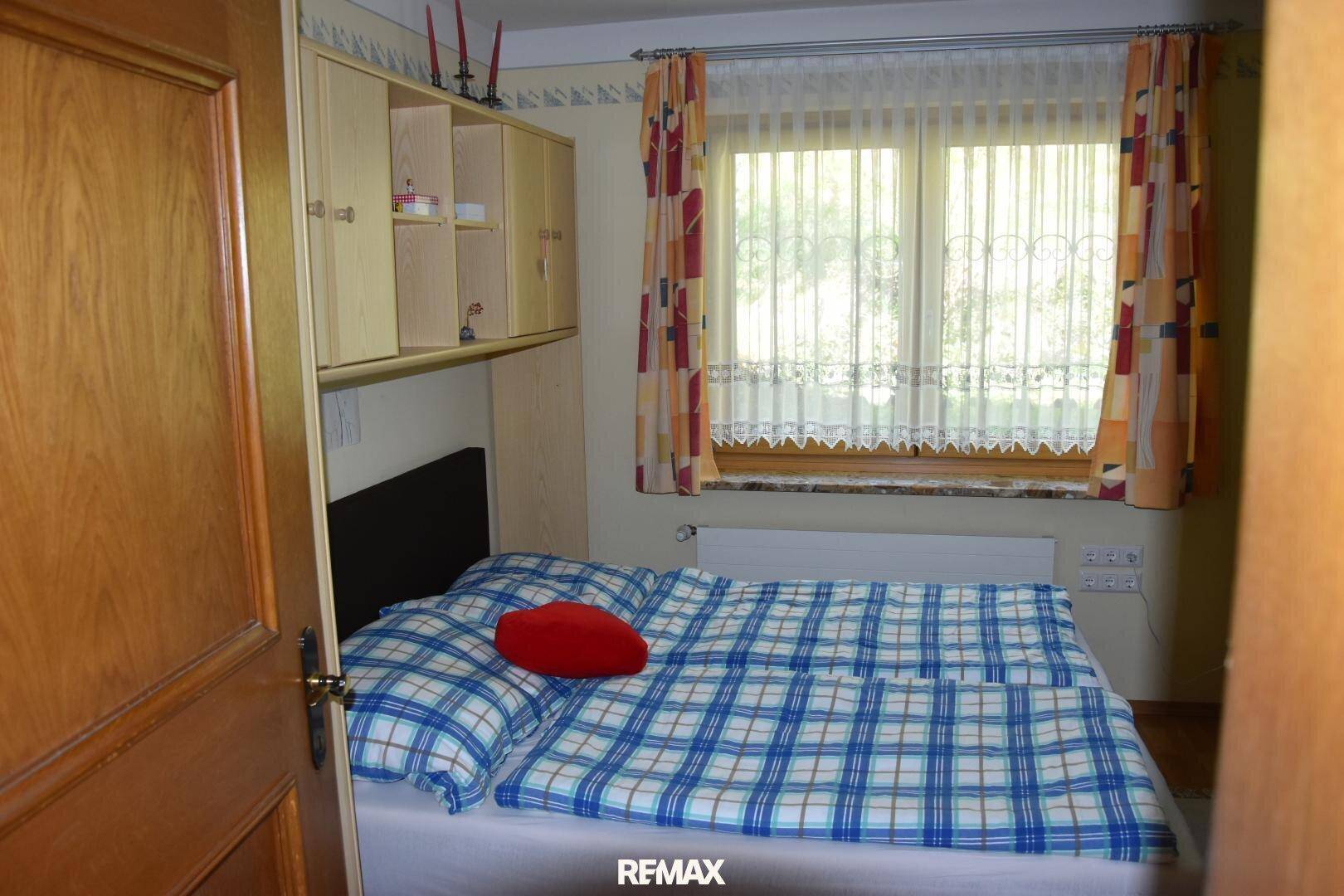 Schlafzimmer mit Doppelbett, Einbauschränken über dem Bett und einem Fenster mit Vorhängen.