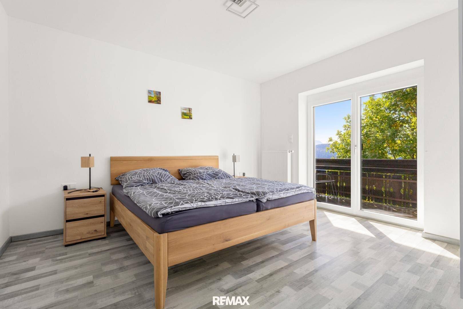 Schlafzimmer mit Holzbett und großem Fenster, das Zugang zu einem Balkon bietet.