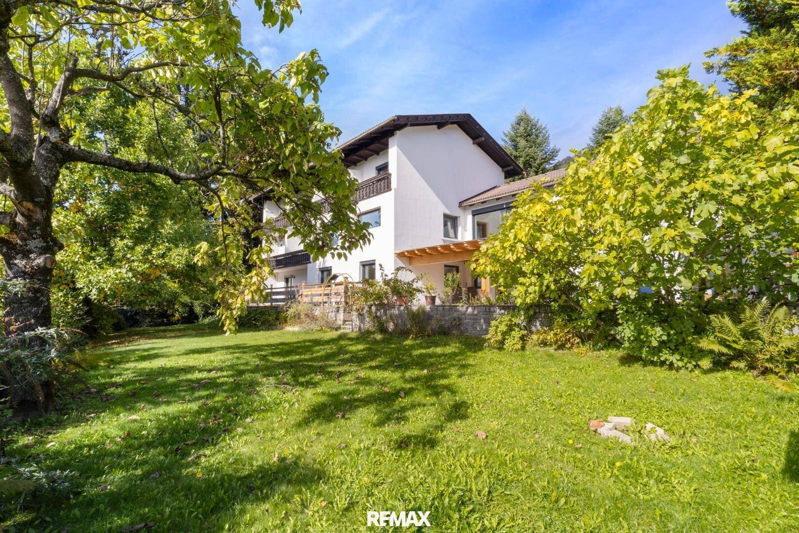 Das Haus vom gepflegten Garten aus gesehen, umgeben von altem Baumbestand.