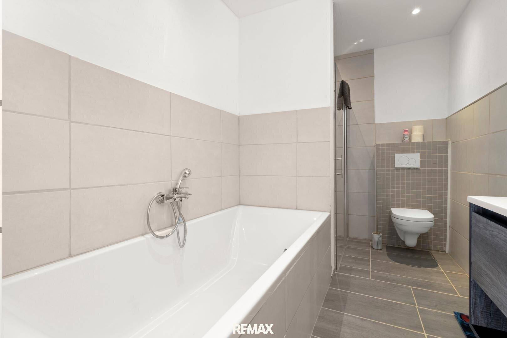 Badezimmer mit Badewanne, Duschbereich und wandhängendem WC in neutralen Farbtönen.
