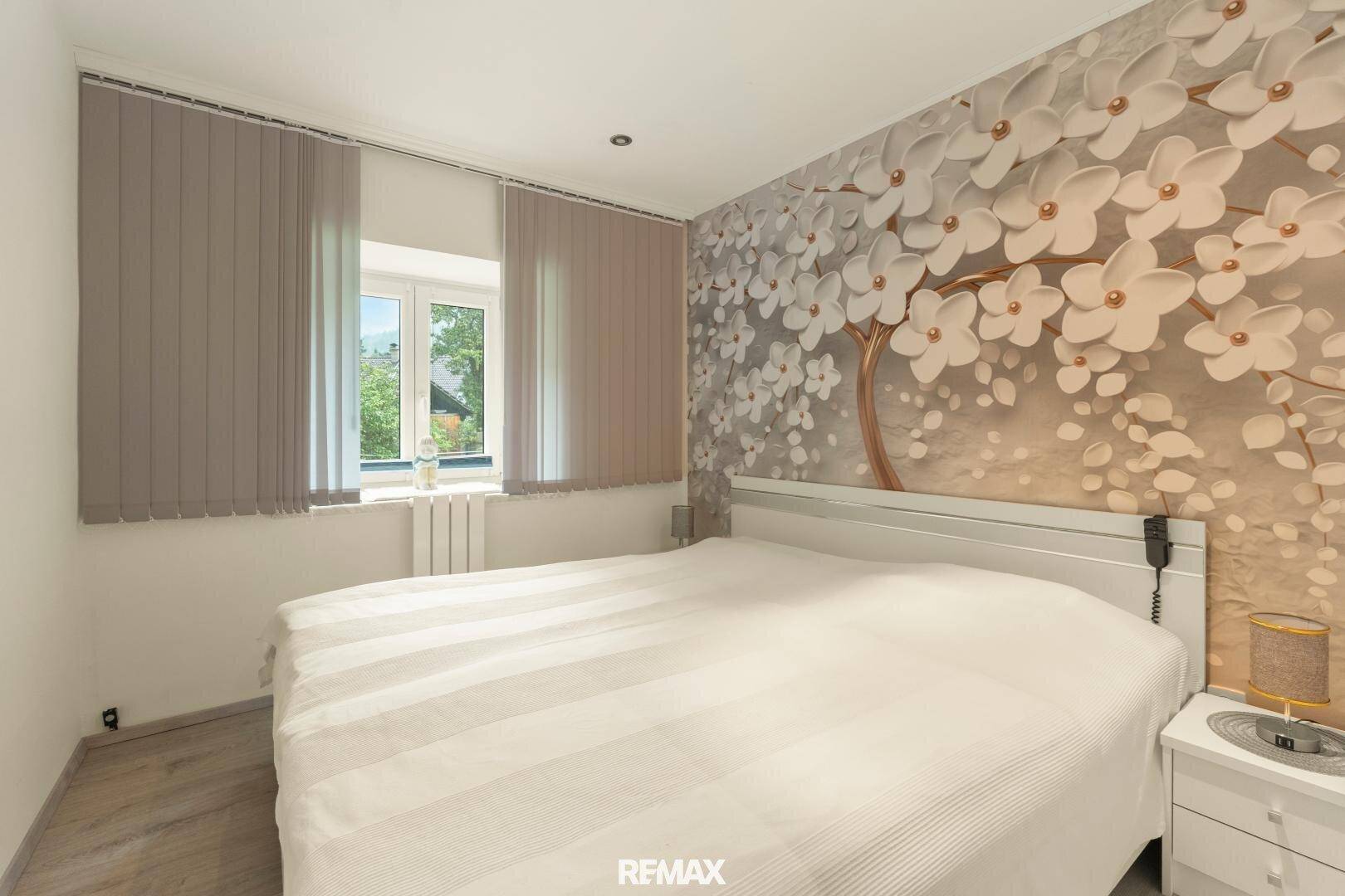 Schlafzimmer mit großem Bett und einer dekorativen Blumenwandtapete als Akzent.