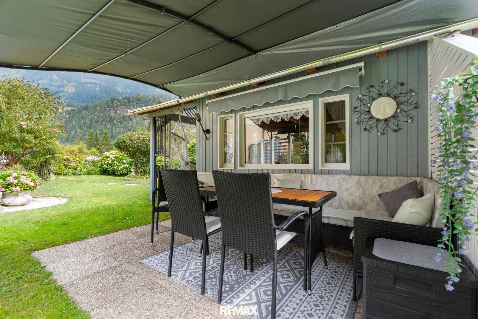 Überdachte Terrasse mit bequemen Sitzgelegenheiten und Blick auf den Garten und die Berge.