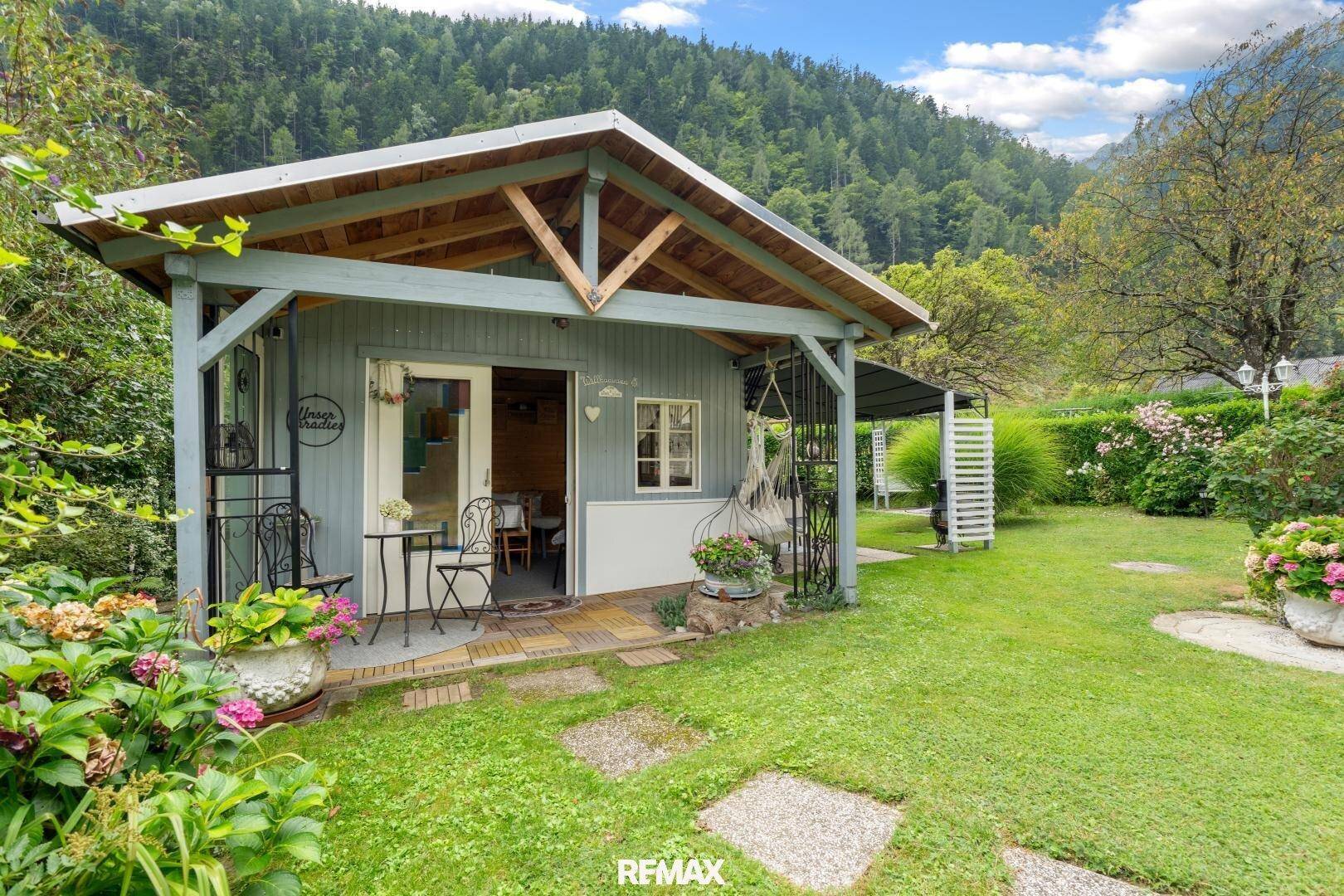 Charmantes Gartenhaus mit überdachter Veranda und Sitzgelegenheiten im grünen Garten.