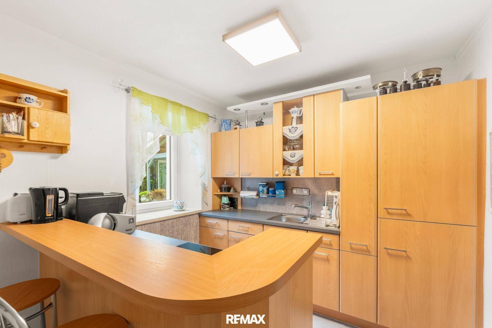 Funktionale Küche mit Holzschränken, Frühstücksbar und Fenster für natürliches Licht.