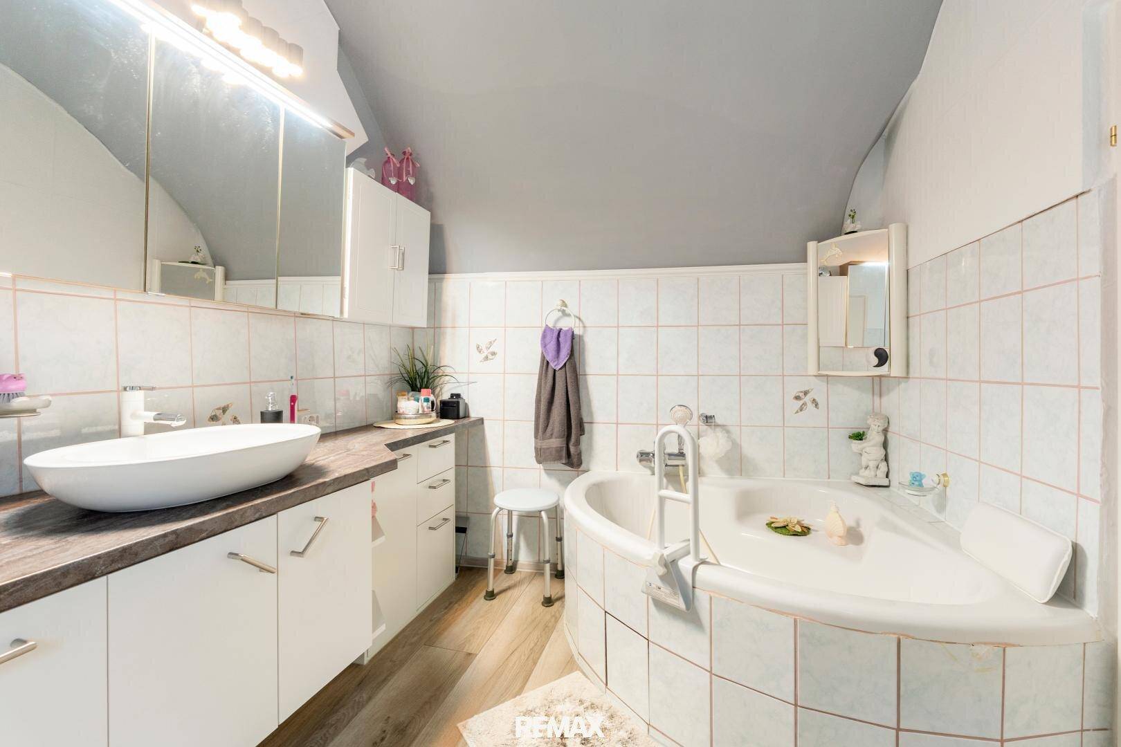 Helles Badezimmer mit Eckbadewanne, Einzelwaschbecken und gefliesten Wänden unter Dachschräge.