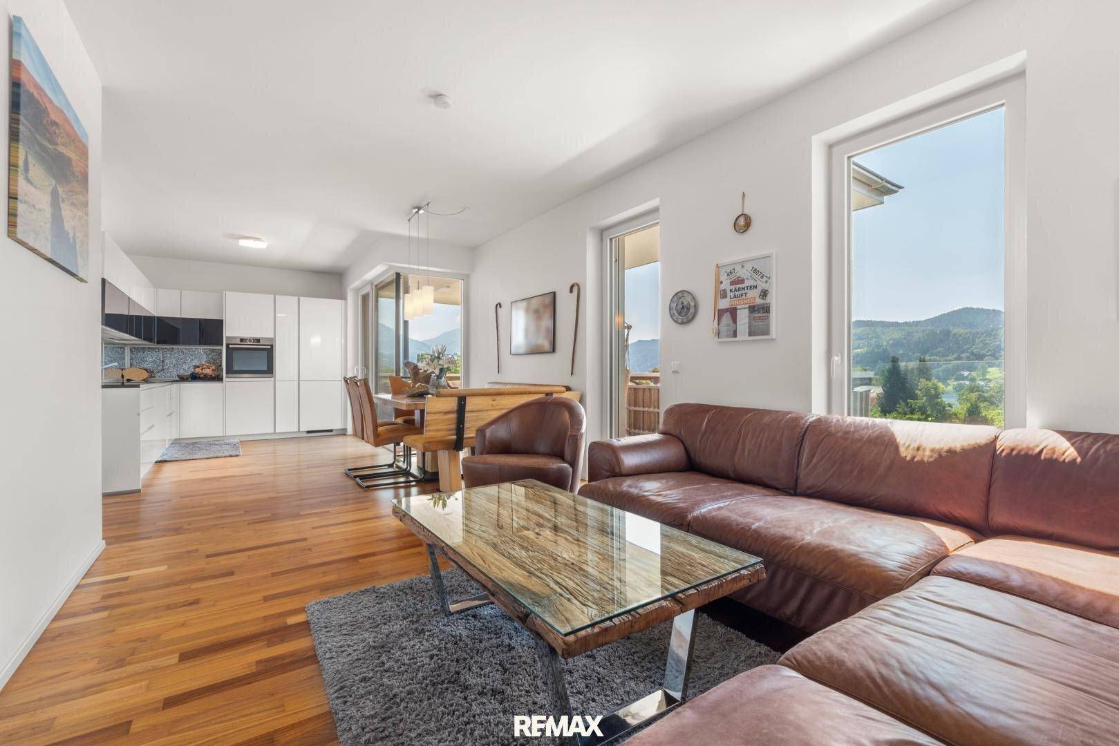 Heller offener Wohn-Essbereich mit moderner Küche, Holzboden und Zugang zum Balkon.